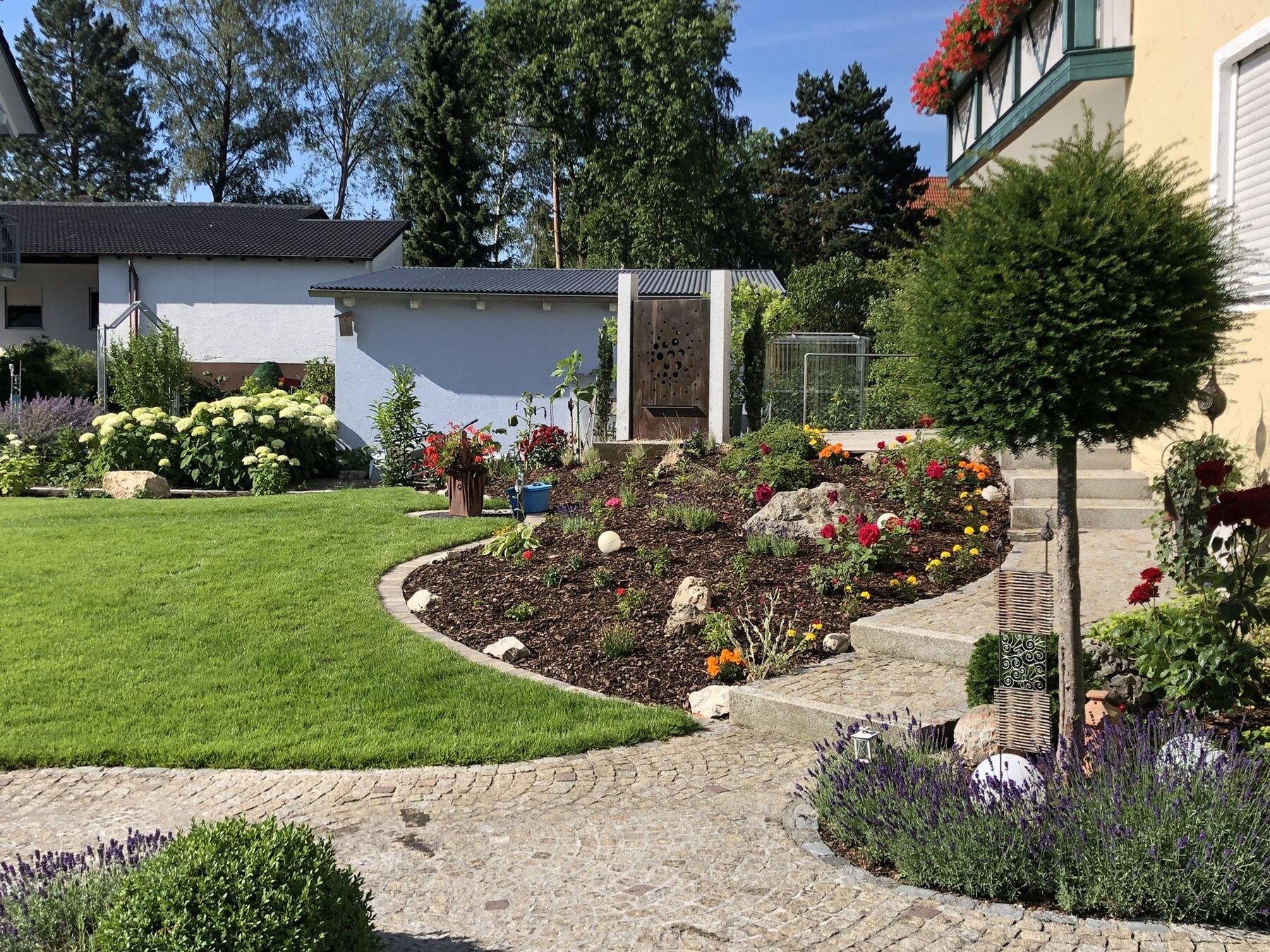 Frisch verlegter Rasen mit geschwungenem Blumenbeet und Kiesweg