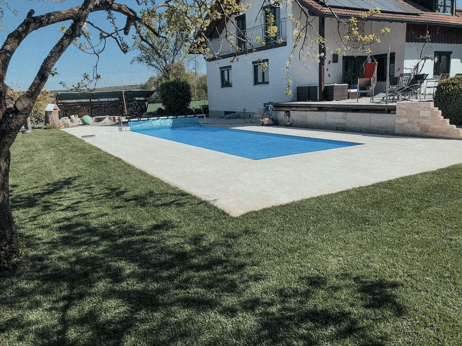 Pool mit hellem Natursteinrand in einem Garten mit Rasen und Bäumen